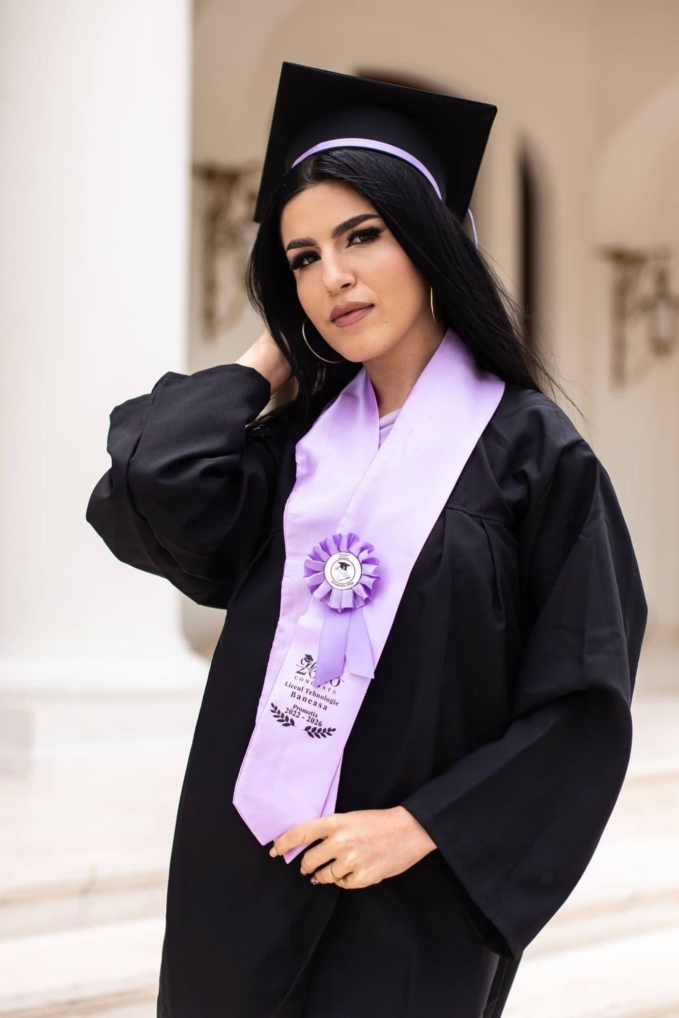Absolventă cu tocă și eșarfă lila, zâmbind