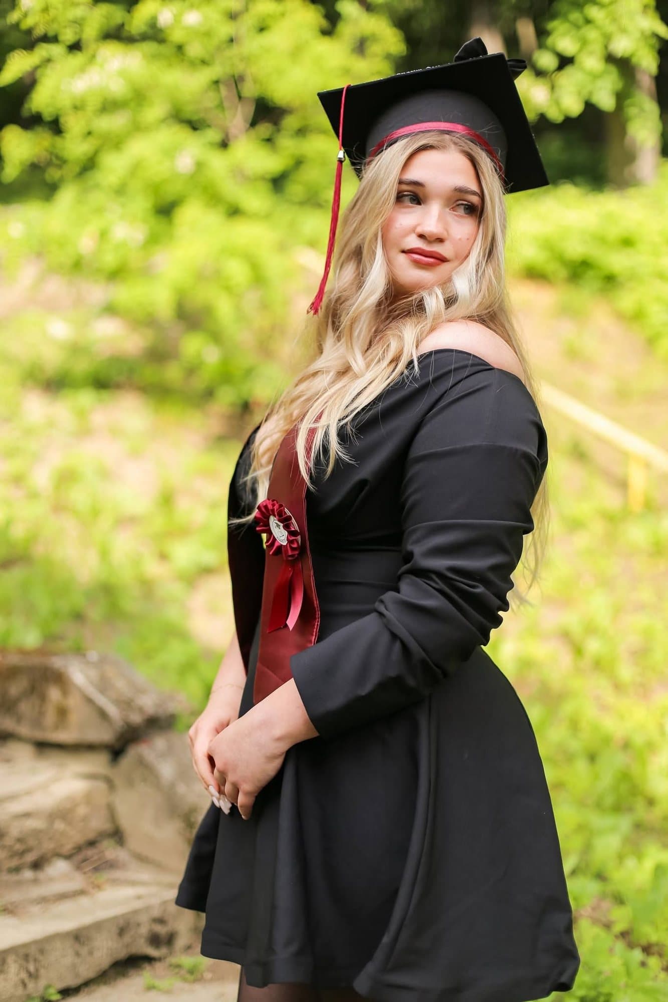 Absolventă în rochie neagră cu eșarfă bordo, în parc